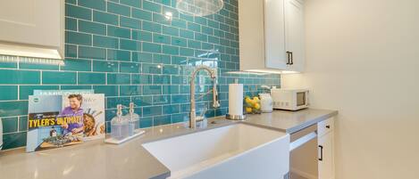 Une cuisine moderne avec un dosseret de couleur turquoise, des armoires blanches et un évier en acier inoxydable.