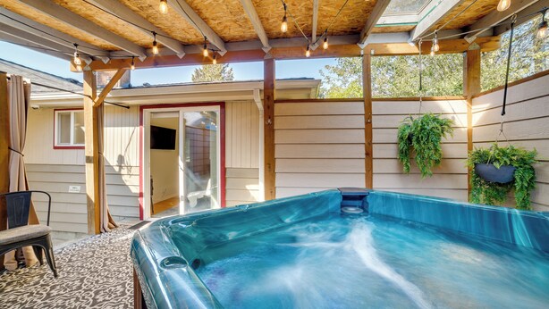 Ett bubbelbad under en träpergola med hängande lampor, omgivet av träväggar och krukväxter.