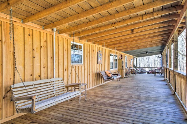 A wooden deck with benches and a swing, wooden walls, and a ceiling fan.