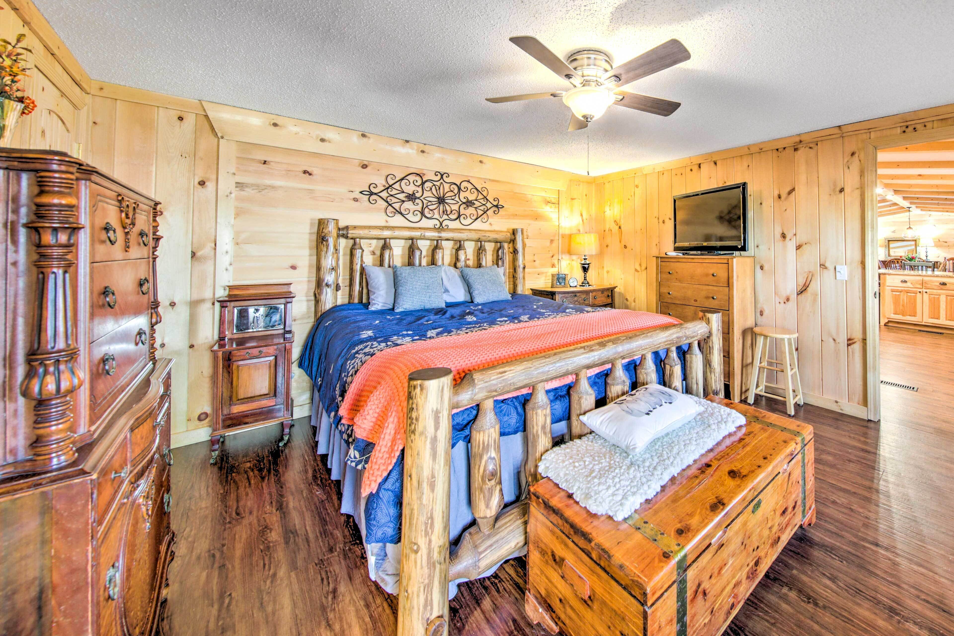 A wooden-paneled bedroom with a bed, dresser, TV, and a ceiling fan.