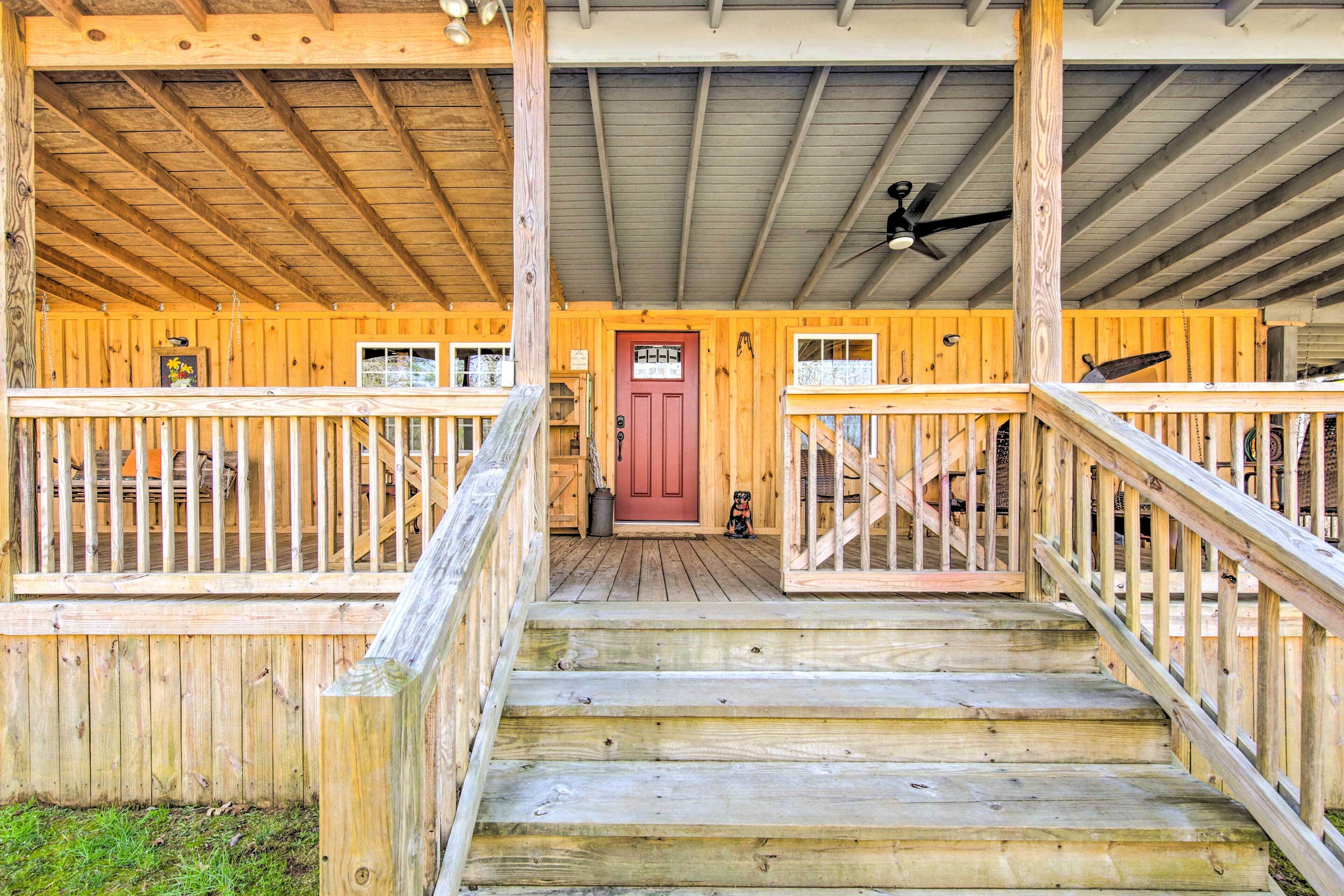A wooden cabin with a porch, a red door, and a staircase leading to the entrance.