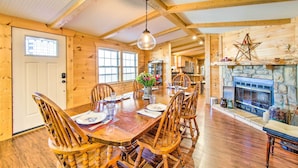 A wooden dining room with a large table and chairs, a stone fireplace, and a wooden ceiling.