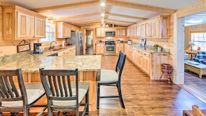 A spacious kitchen with wooden cabinets, granite countertops, and a central island with chairs.