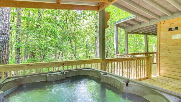 A hot tub with a wooden deck and a view of a forest.