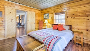 A wooden cabin bedroom with a bed, a nightstand, a lamp, and a bench.