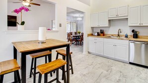 A modern kitchen with white cabinets, a wooden dining table, and bar stools. - Peaceful Savannah Home - 11 Mi to Beaches! (Savannah)
