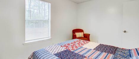Une chambre avec un grand lit, un ventilateur de plafond, une fenêtre avec des stores et un fauteuil rouge.