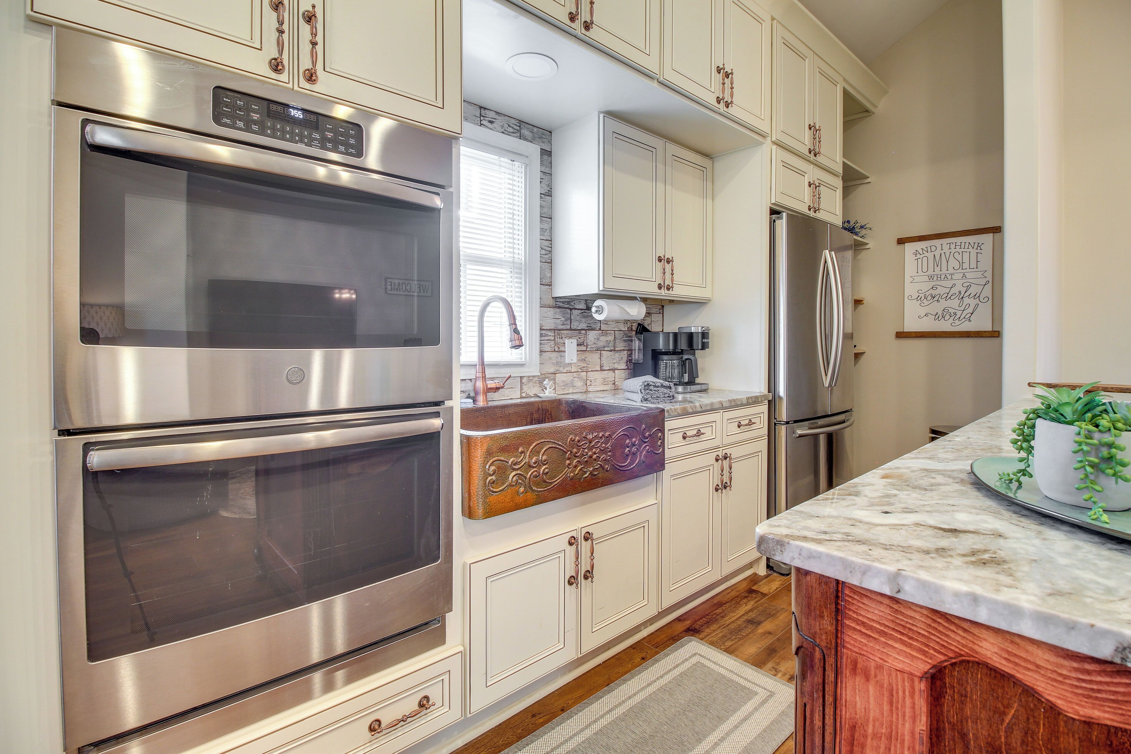 A kitchen with stainless steel appliances, white cabinetry, and a marble countertop.
