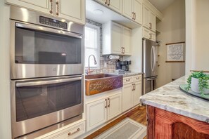 Una cocina con electrodomésticos de acero inoxidable, muebles blancos y encimera de mármol.