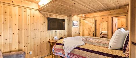 Un dormitorio de cabaña de madera con una cama, una silla, una mesita de noche y un televisor.