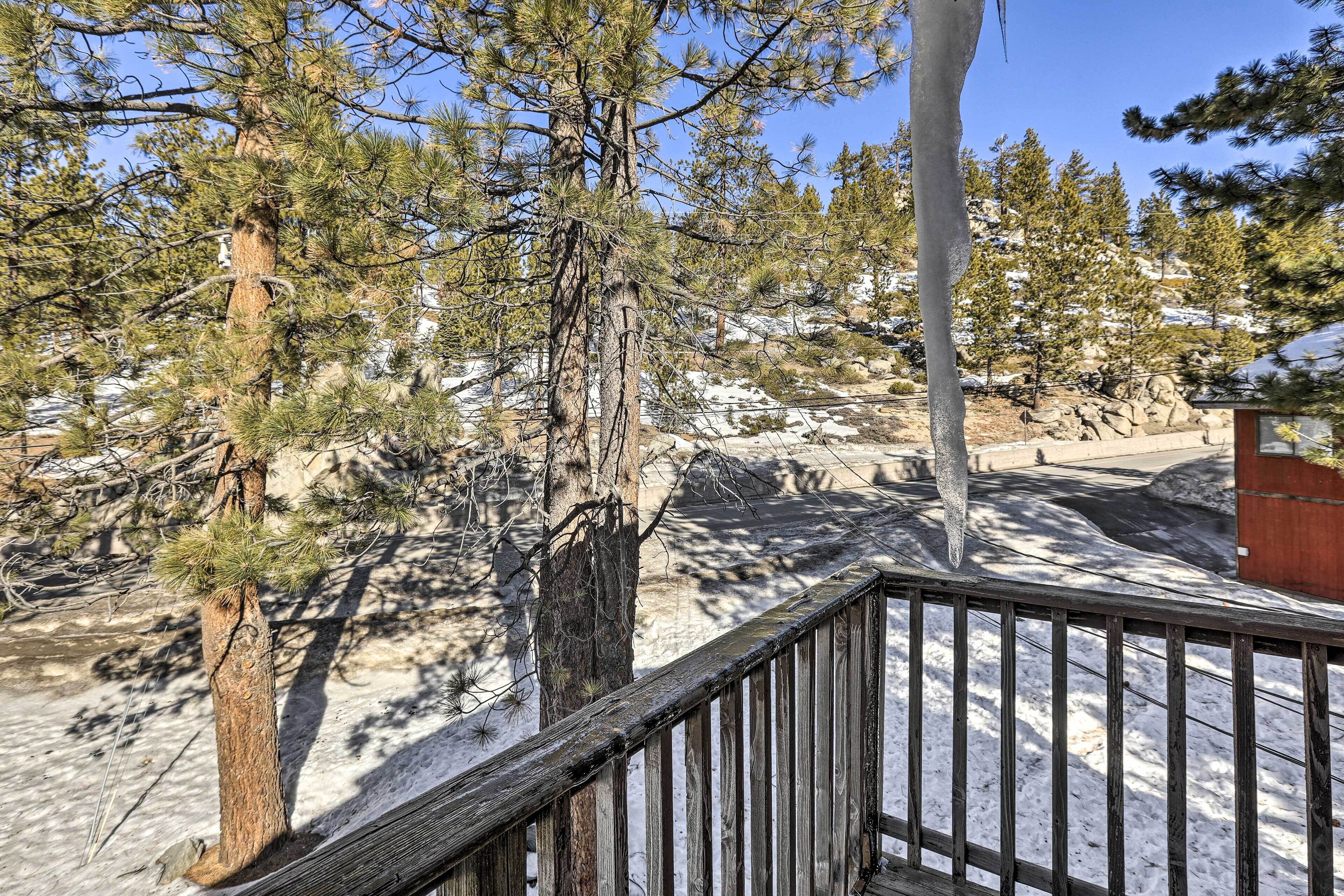 A wooden deck with a railing overlooking a snowy landscape with trees.