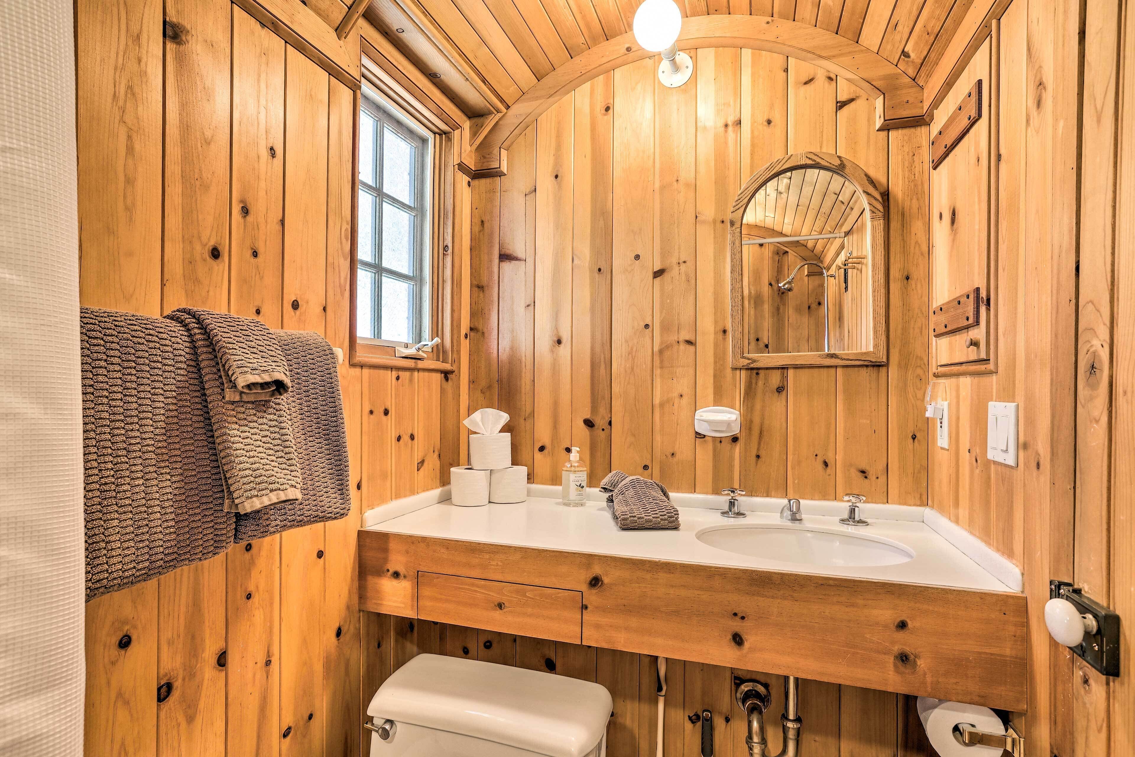 A wooden bathroom with a sink, mirror, towel rack, and toilet.