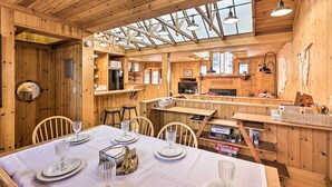 Interior de una cabaña de madera con comedor, cocina y ventanas amplias.