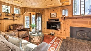 Interior acogedor de una cabaña de troncos con chimenea, muebles de cuero, un televisor grande y techo de madera.
