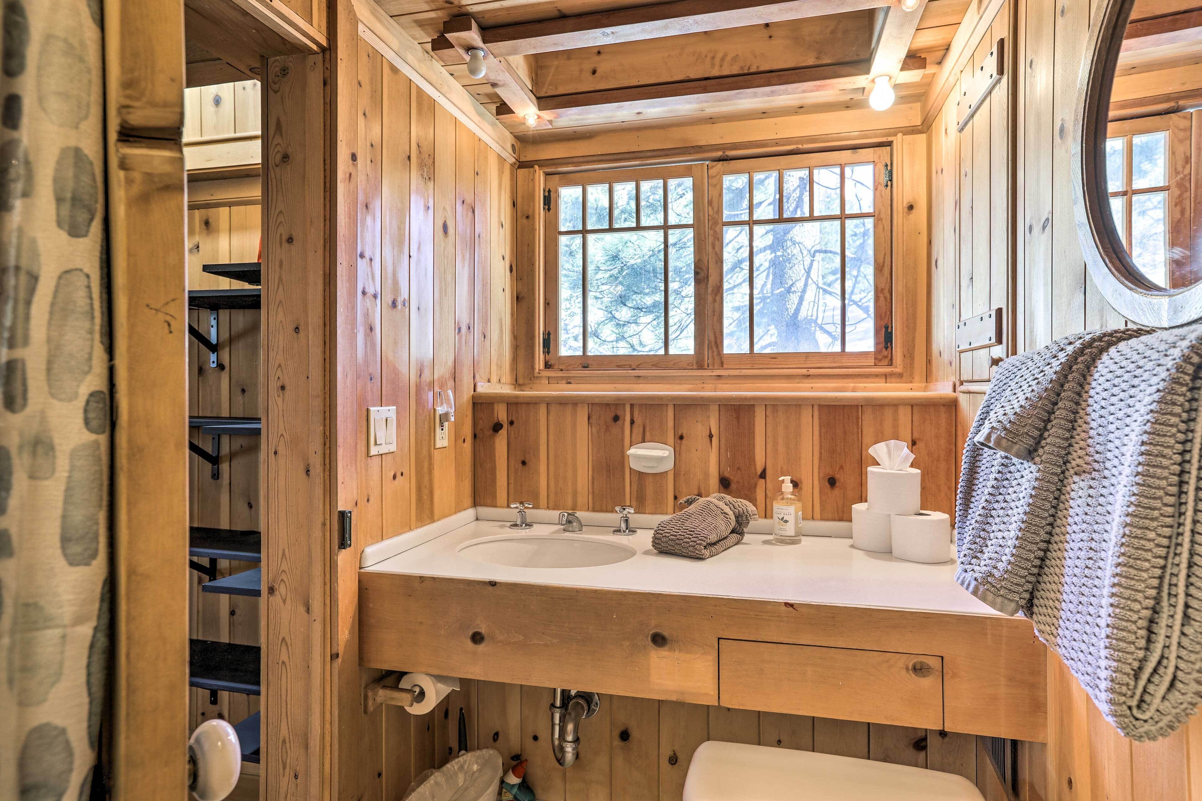 A wooden cabin bathroom with a large window, a sink, and a towel hanging on the wall.