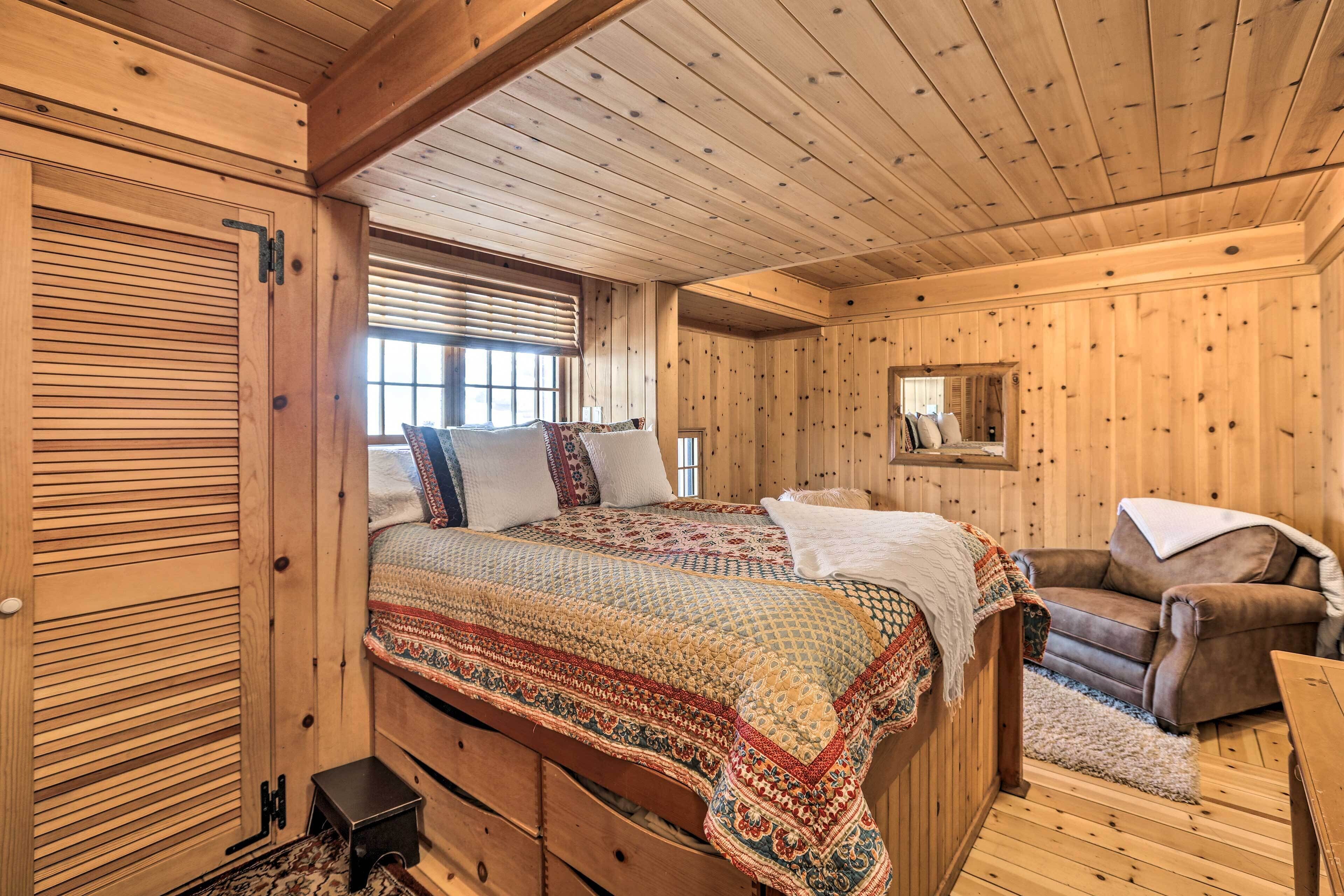 Un dormitorio de cabaña de madera acogedor, con una cama grande, una silla y una mesita.