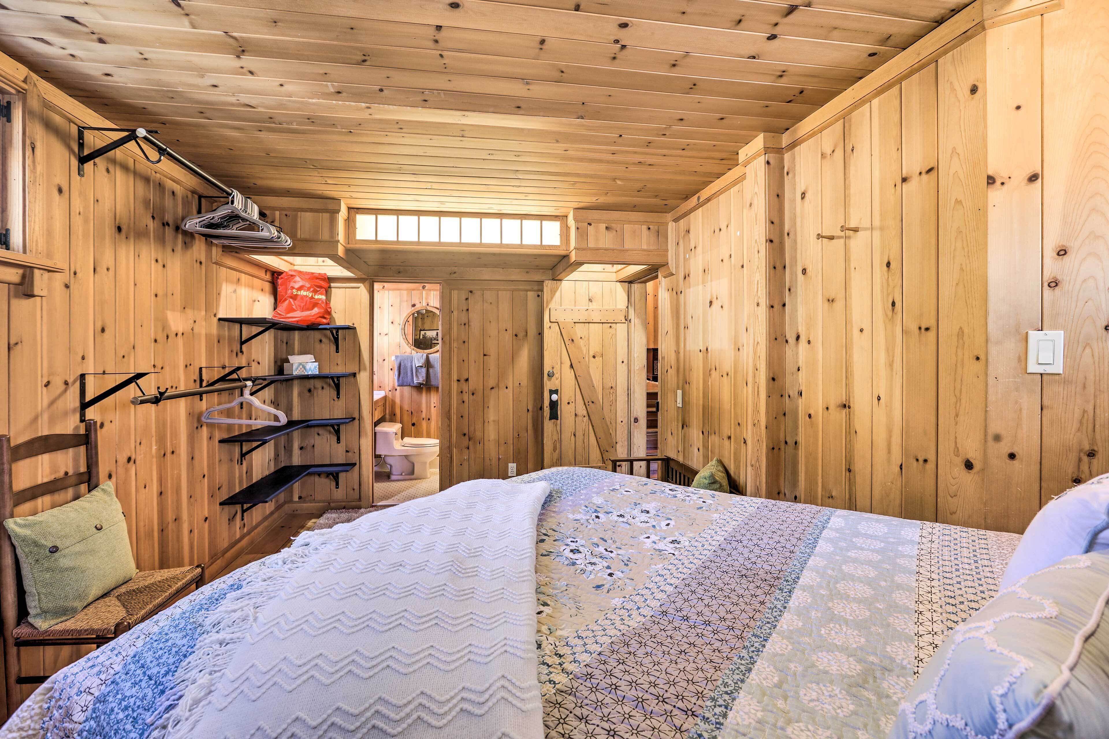 Una camera da letto in una baita di legno, con un letto, una sedia, uno scaffale con vestiti appesi e una finestra.