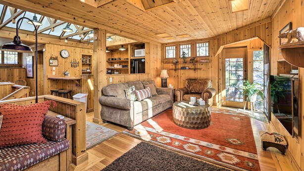 Interior acogedor de una cabaña con techo de madera, un sofá, una zona de comedor y una cocina.