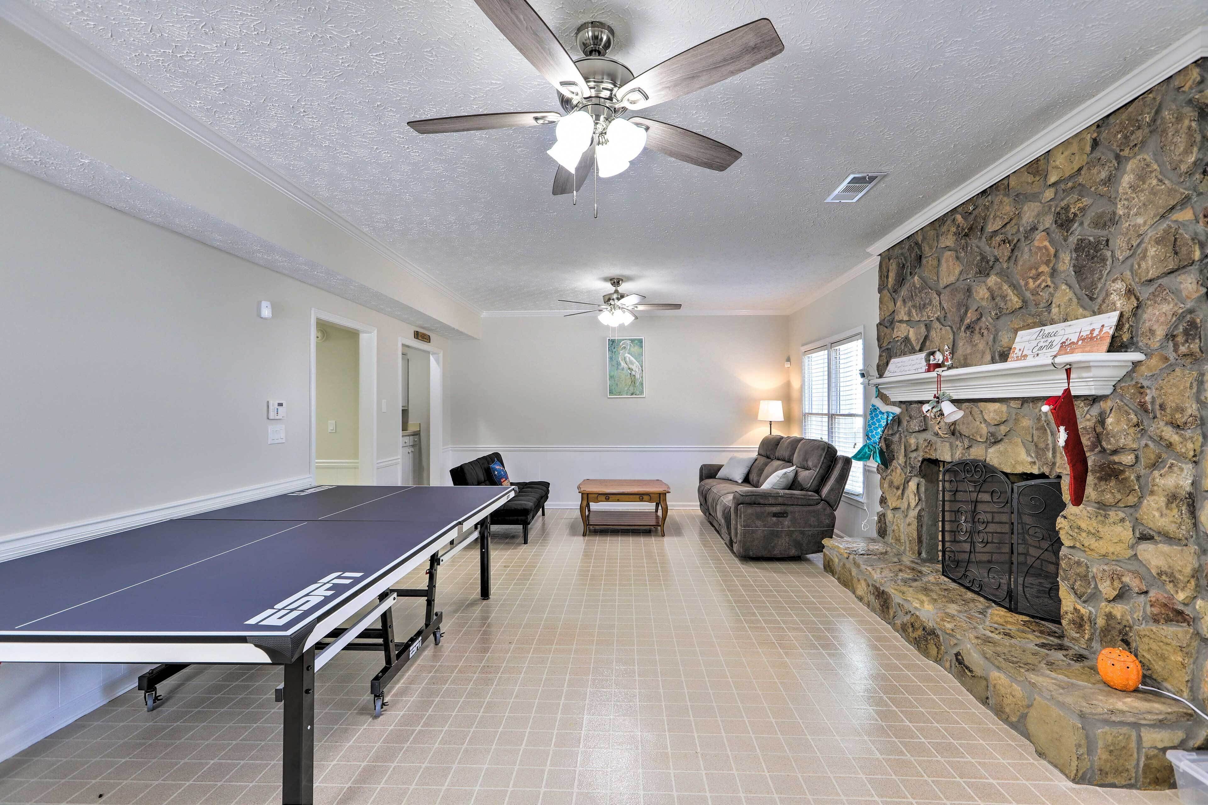 A spacious living room with a ping pong table, a stone fireplace, a ceiling fan, and a comfortable seating area.