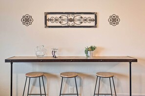 A bar area with a long table, three stools, decorative wall art, a pitcher, a candle holder, and a small plant. - Sunny Tucson Abode w/ Fire Pit 9 Mi to U of A (Tucson)