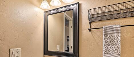 Een badkamer met een witte wastafel, een grote spiegel en een handdoekrek met decoratieve handdoeken.