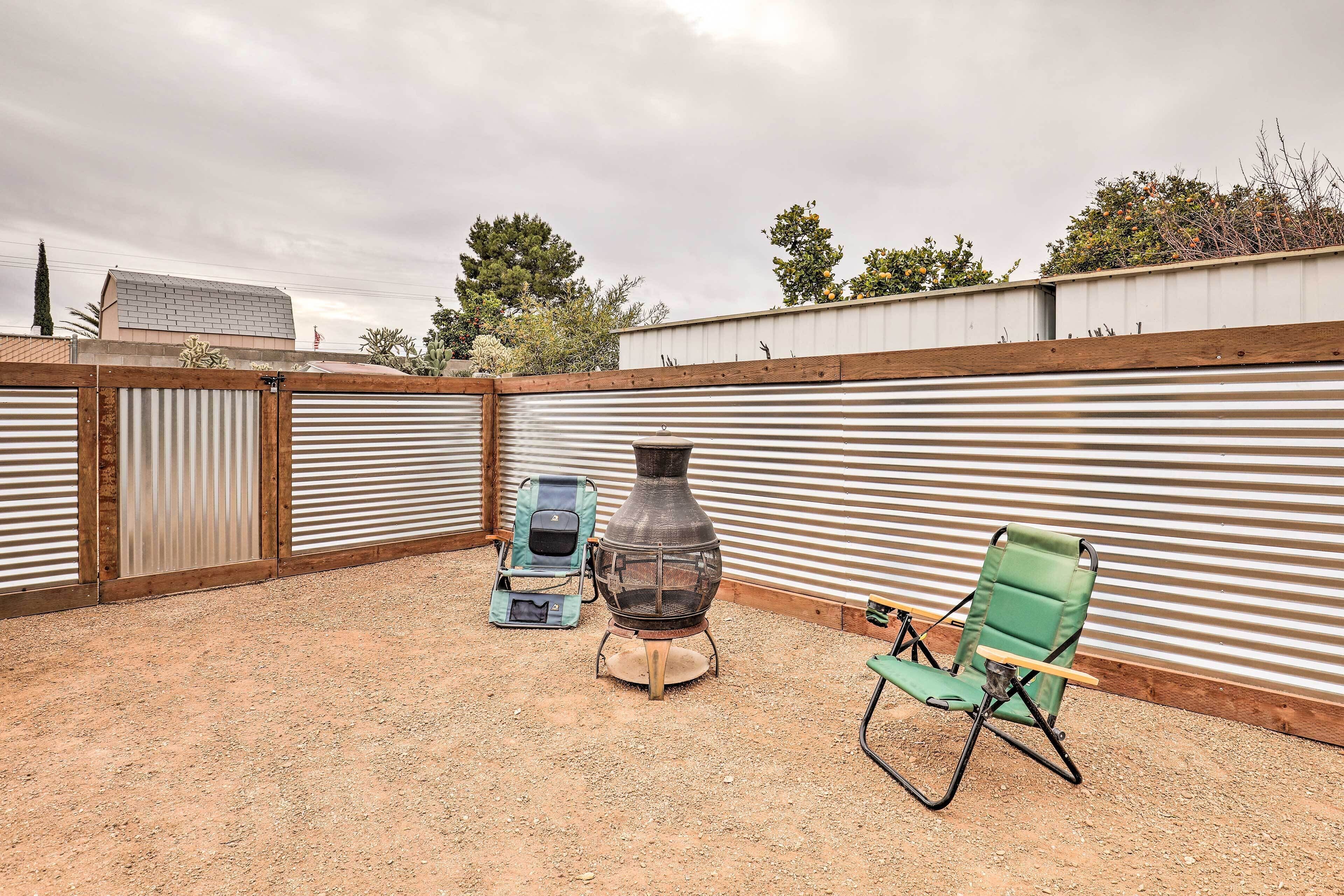 A patio area with a metal fence, a green folding chair, and a portable grill.