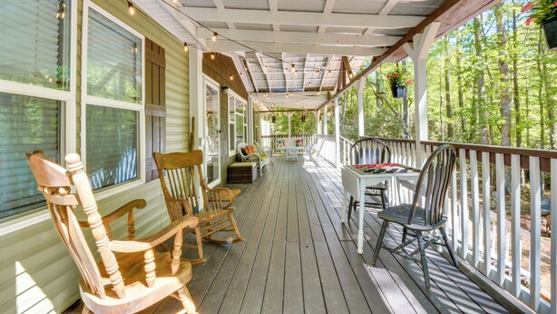 A covered porch with wooden chairs, a table, and hanging plants.
