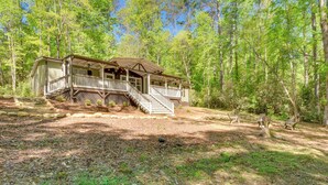 A cabin with a porch, steps, and a deck, surrounded by trees.