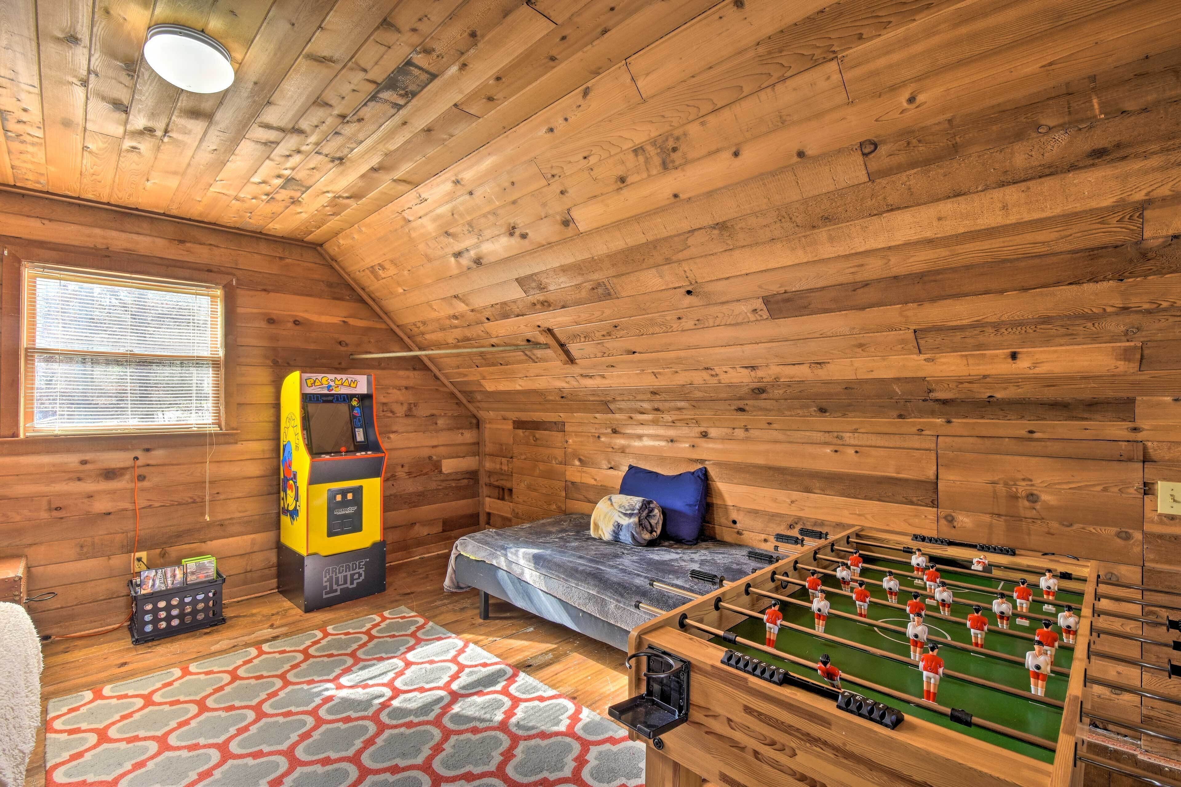 Une pièce chaleureuse aux murs en bois, avec un lit orné d’un coussin bleu, une table de baby-foot et une console de jeux Nintendo 64.