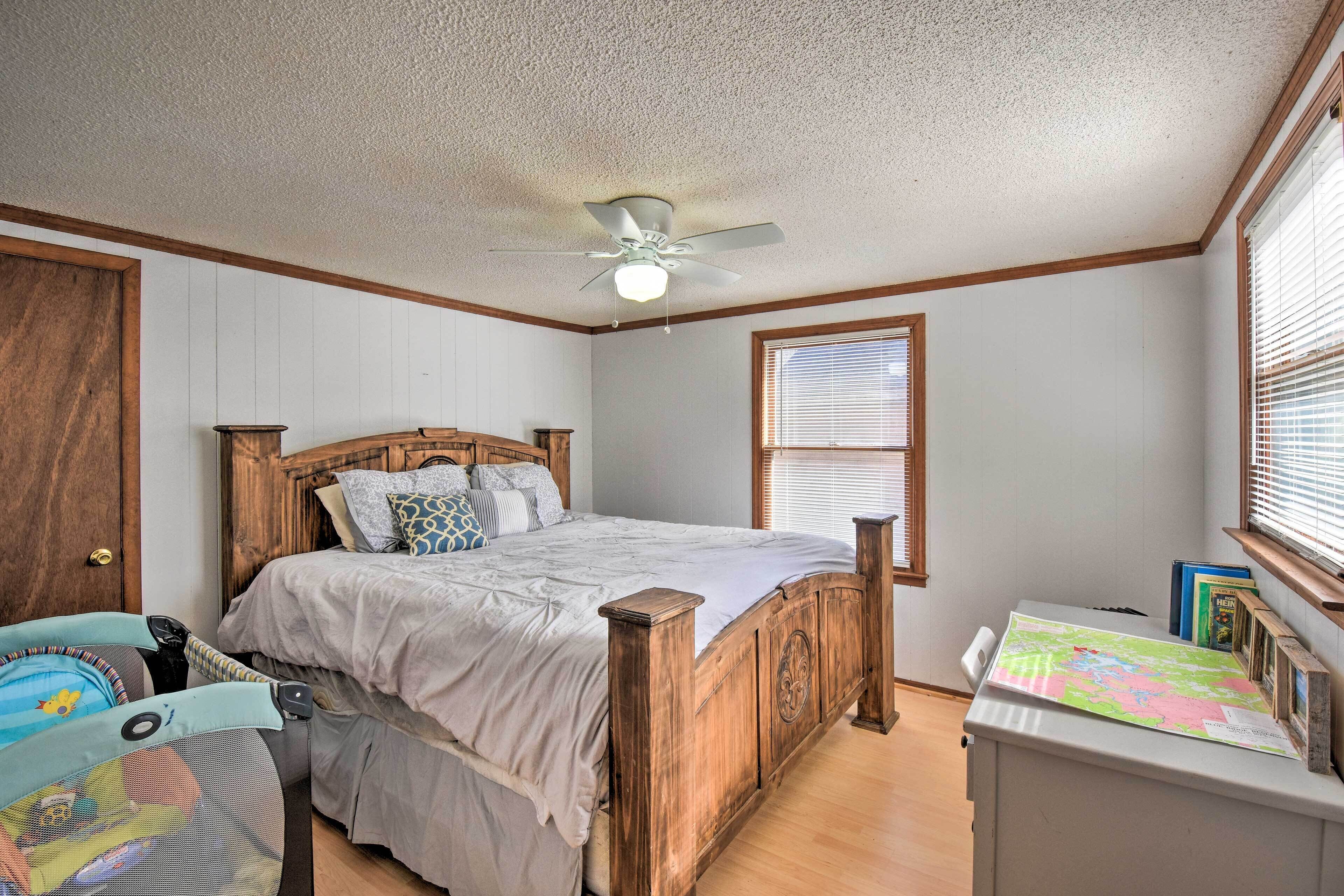 A bedroom with a wooden bed, a ceiling fan, a window with blinds, and a desk with a map.