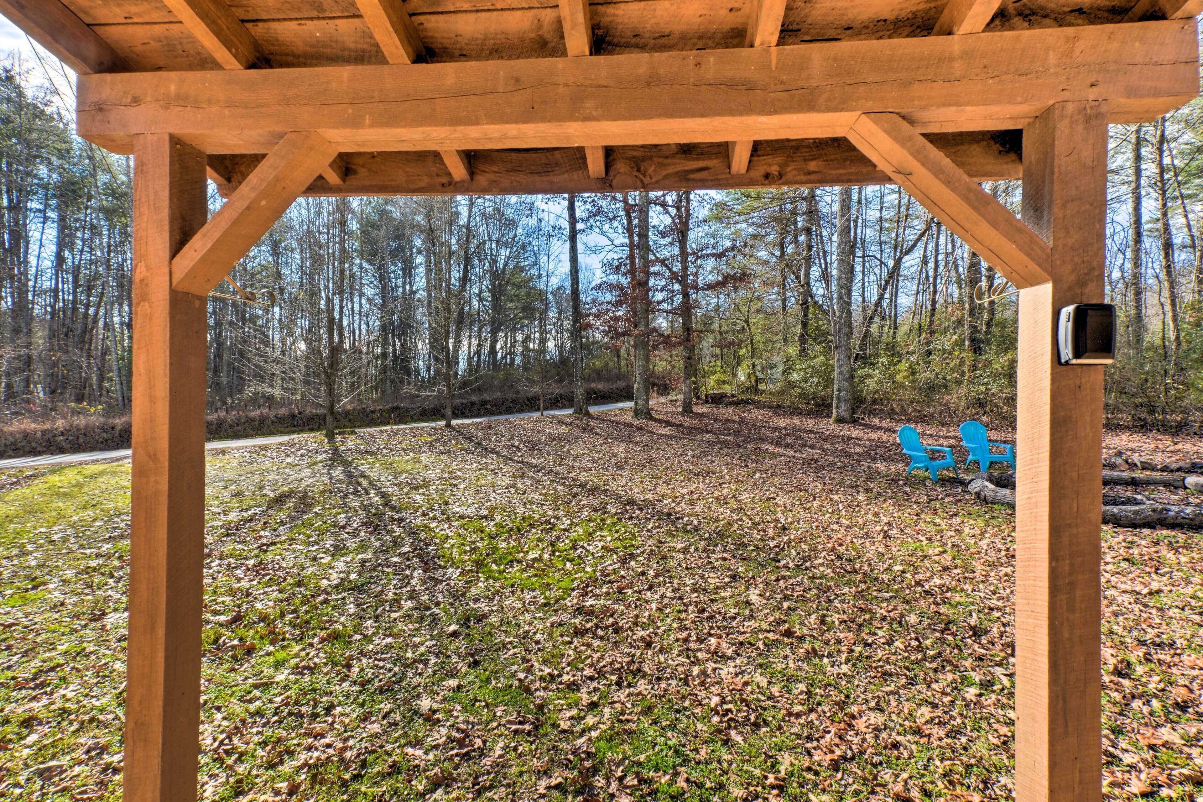 A wooden gazebo with a view of a forested area and a bench with chairs.