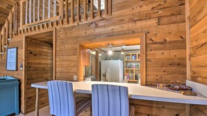Interior de una cabaña de madera con una cocina que incluye una encimera blanca, dos sillas a rayas y un refrigerador.