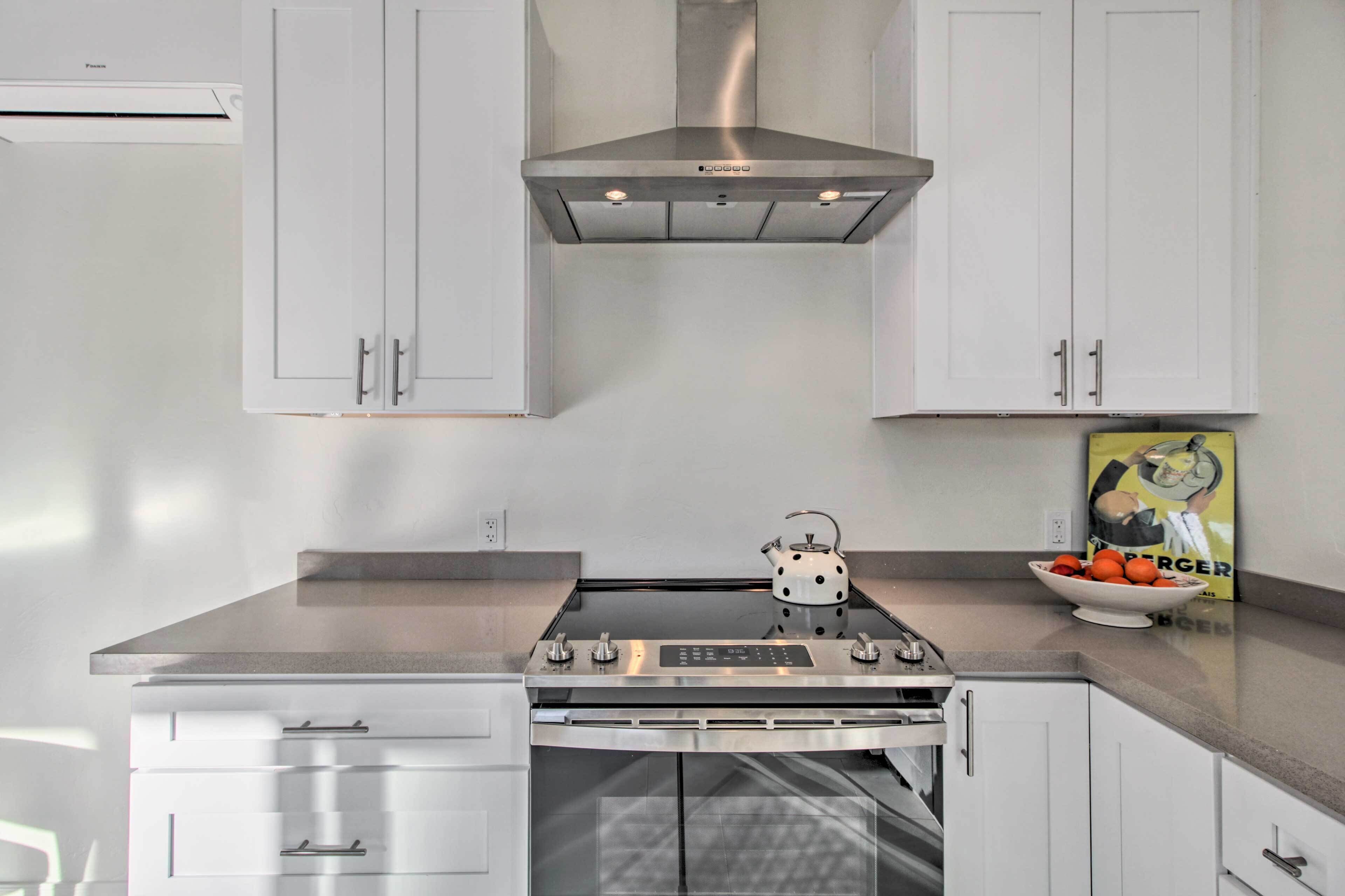 A modern kitchen with white cabinetry, a stainless steel range hood, a built-in oven, and a kettle on the countertop.