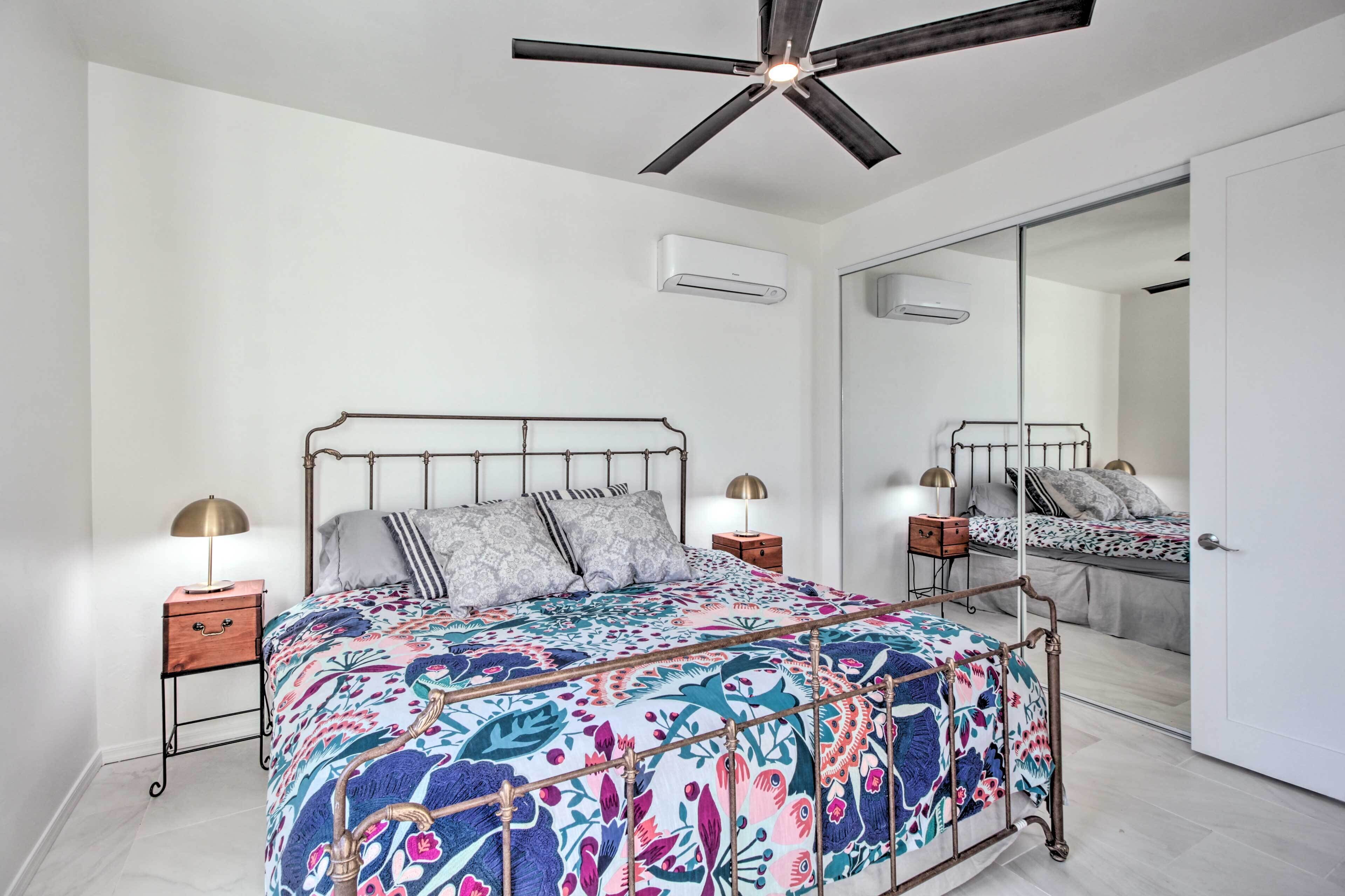 Un dormitorio con cama, mesitas de noche, ventilador de techo, espejo y aire acondicionado.
