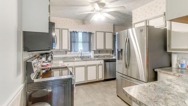 A kitchen with stainless steel appliances, white cabinets, a marble countertop, and a ceiling fan. - Cozy Waycross House w/ Yard & Screened Patio! (Waycross)