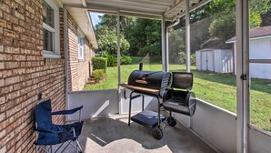 A covered patio with a grill, a folding chair, and a view of a backyard. - Cozy Waycross House w/ Yard & Screened Patio! (Waycross)