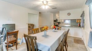 A dining area with a table set for four, surrounded by wooden chairs. A ceiling fan is visible above the table, and there is a television on a stand to the left. - Cozy Waycross House w/ Yard & Screened Patio! (Waycross)