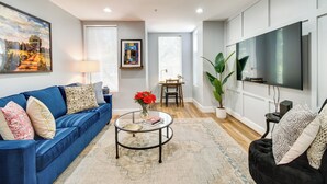 A modern living room with a blue sofa, a round coffee table, a TV, and a large window.