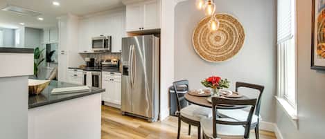 A modern kitchen with white cabinets, stainless steel appliances, and a dining area with a round table and chairs.
