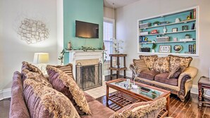 Een woonkamer met een open haard, een aan de muur bevestigde televisie en een boekenplank vol boeken en decoratieve objecten.