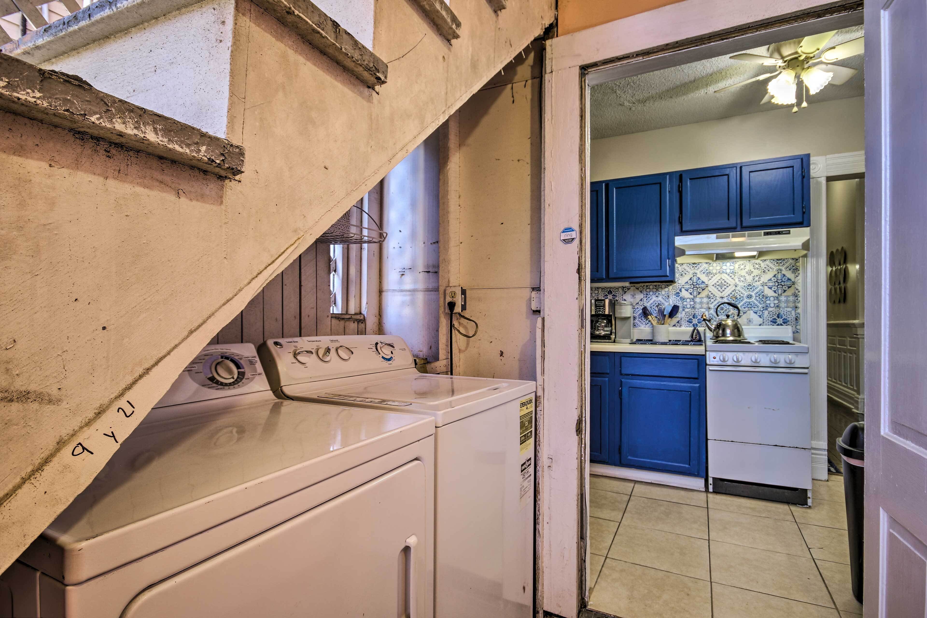 Un espace buanderie équipé d’un lave-linge et d’un sèche-linge, une cuisine avec des armoires bleues et une cuisinière, et un ventilateur de plafond.