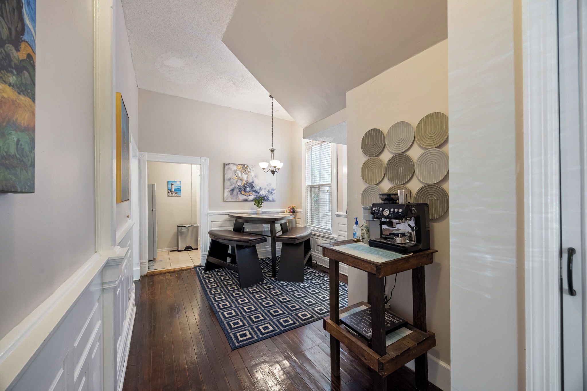 A modern kitchen with a dining area, a coffee machine, and a patterned rug.