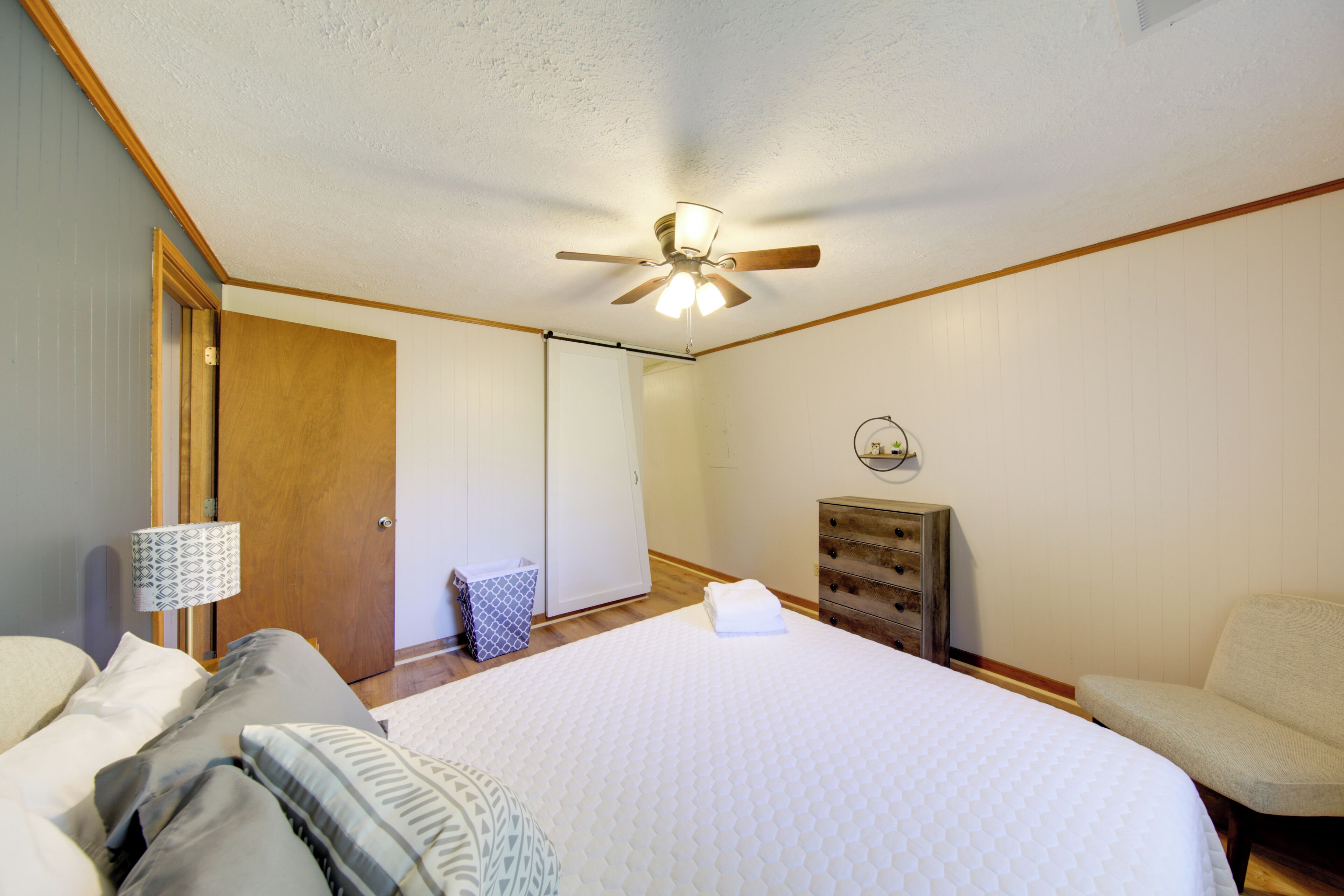 A bedroom with a bed, a ceiling fan, a dresser, a chair, and a lamp.
