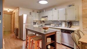 A kitchen with wooden cabinets, a central island, stools, a dishwasher, and a microwave. - Pet-friendly Ellijay Cabin in the Woods on 1 Acre! (Ellijay)
