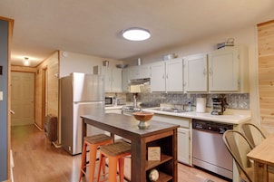 Una cocina con armarios de madera, una isla central, taburetes, lavavajillas y microondas.