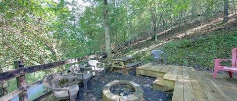 A wooden deck with picnic tables and chairs, surrounded by trees.