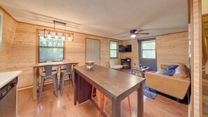 A spacious room with a wooden interior, a dining table with chairs, a sofa, and a television. - Pet-friendly Ellijay Cabin in the Woods on 1 Acre! (Ellijay)