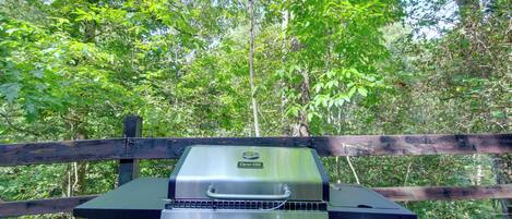 A portable grill with a digital display, set against a backdrop of a wooden fence and lush greenery.