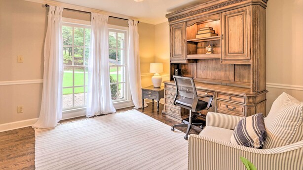 A room with a large window, a wooden cabinet, a desk with a lamp, and a striped sofa. - Family-friendly Athens Escape ~ 2 Mi to Uga! (Athens)