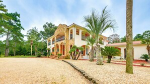 A large, multi-story building with a stone facade, multiple balconies, and a landscaped garden with palm trees and gravel pathways. - Spacious Georgia Vacation Rental w/ Large Deck (Leesburg)